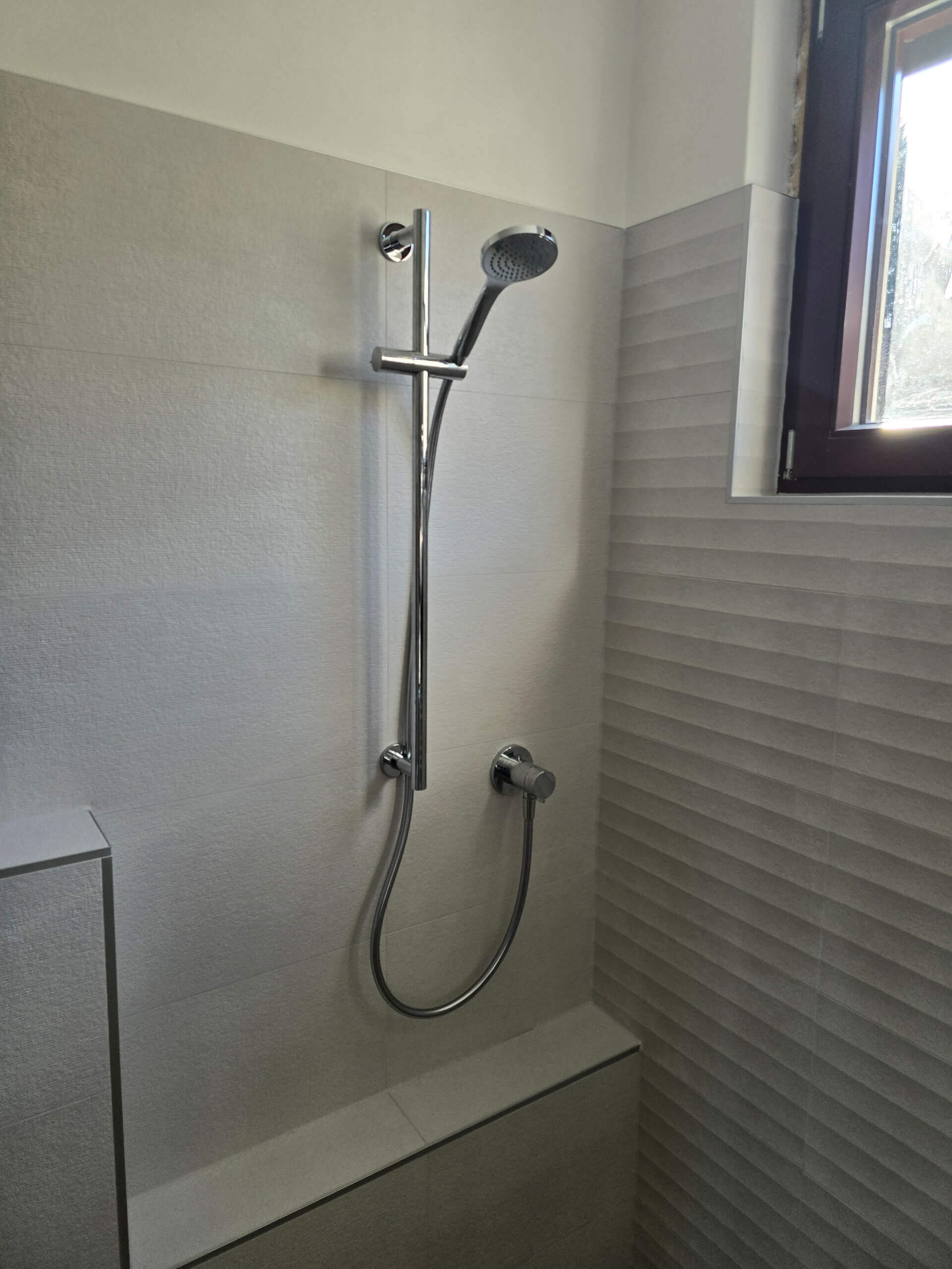 Moderne Dusche mit verstellbarer Duschbrause und eleganten Fliesen, natürlich beleuchtet durch ein Fenster.