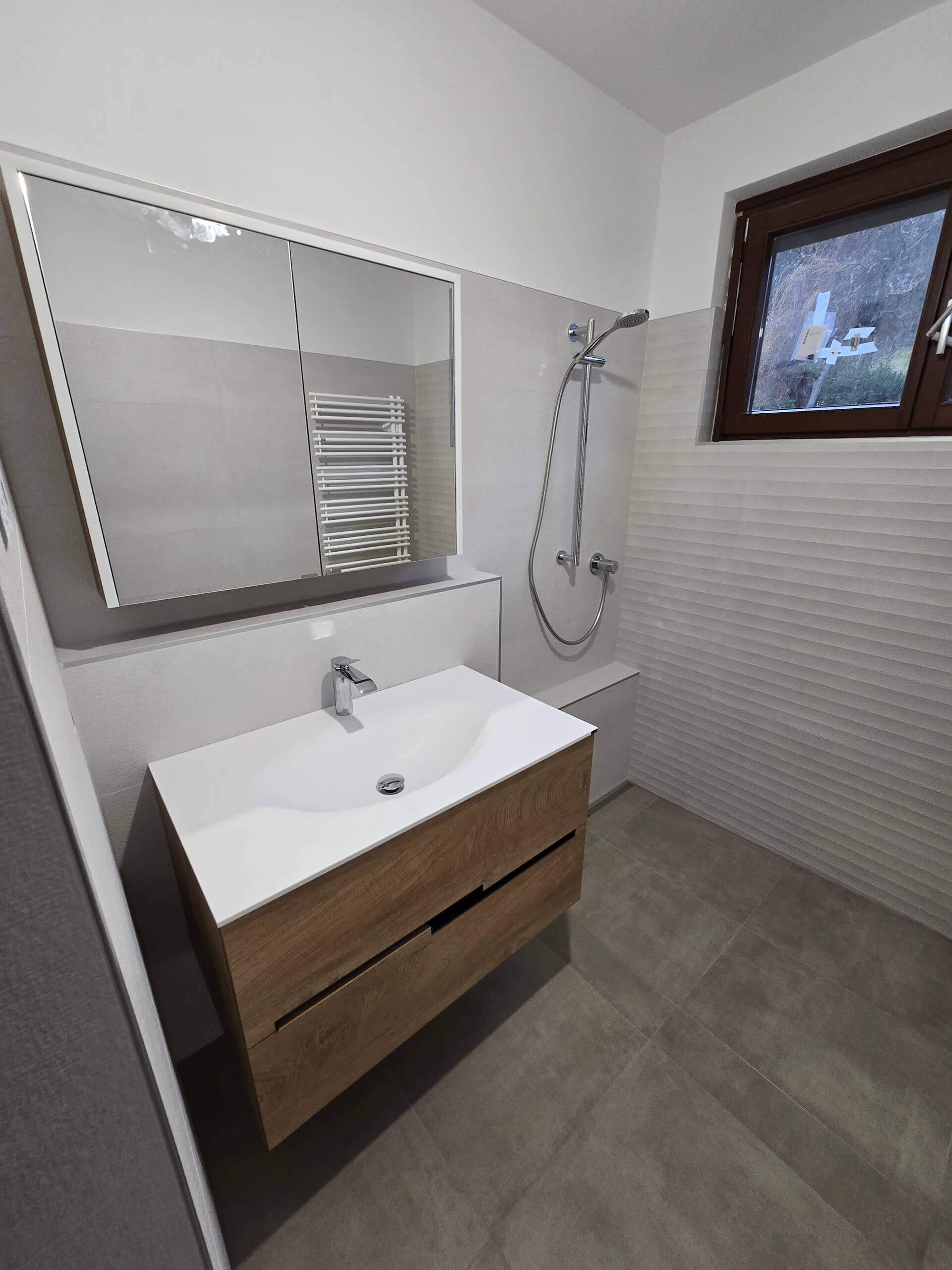 Modernes Badezimmer mit weißem Waschtisch, Spiegel und Dusche, minimalistisches Design, natürliche Holzoptik.