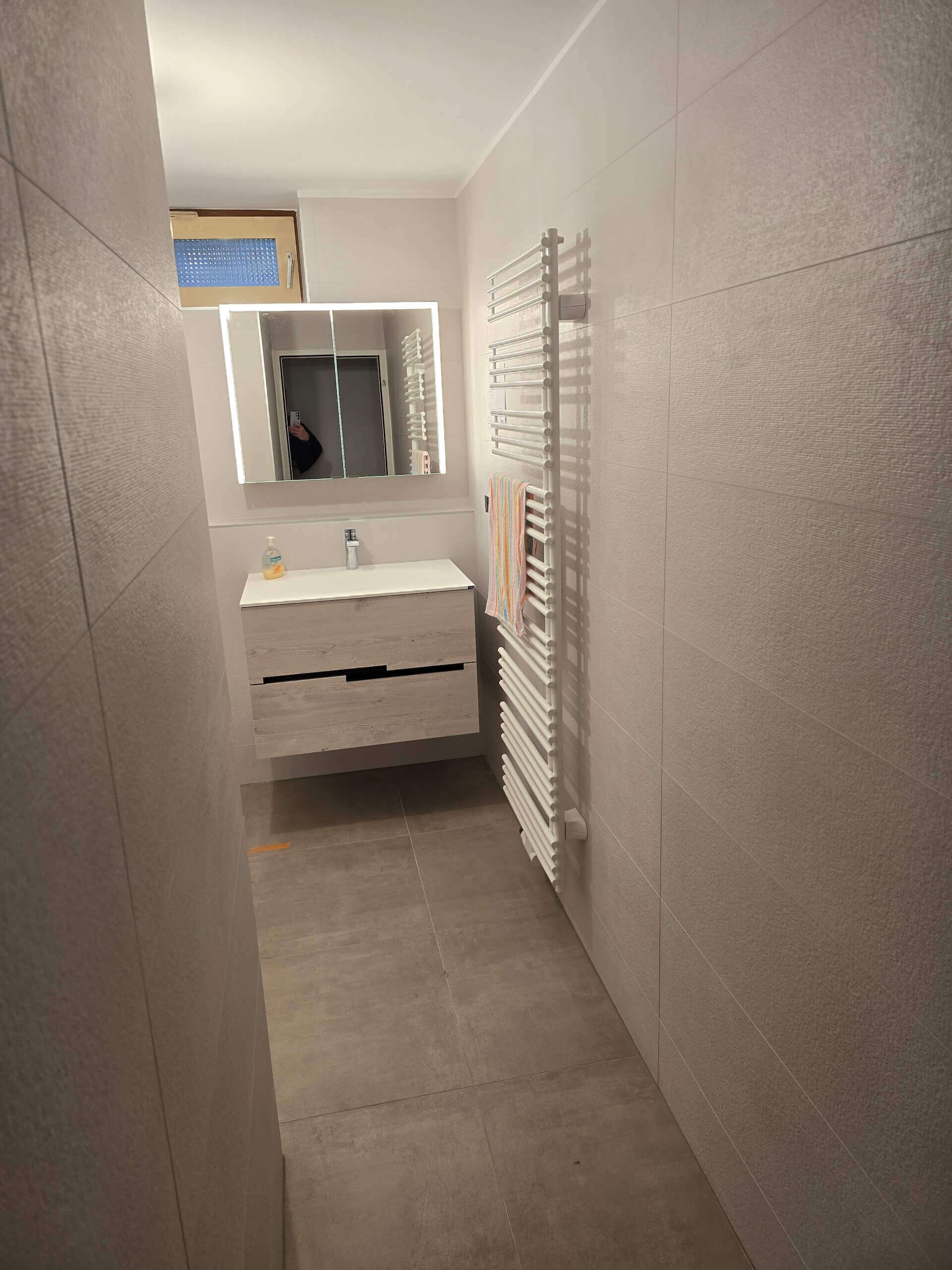 Modernes, minimalistisches Badezimmer mit Wandspiegel, Waschtisch und Heizkörper. Elegantes Design, neutrale Farben.