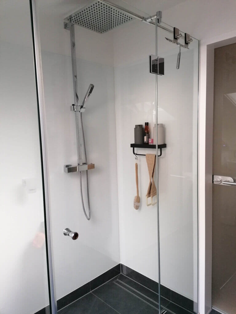 Moderne Duschkabine mit Regenduschkopf und weißen Fliesen, dekoriert mit Duschutensilien auf schwarzem Regal.