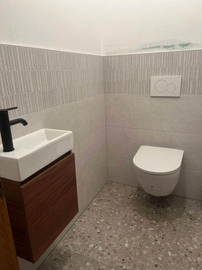 Modernes Gäste-WC mit Hänge-WC und kleinem Waschbecken, minimalistisches Design und dezente Fliesenverkleidung.