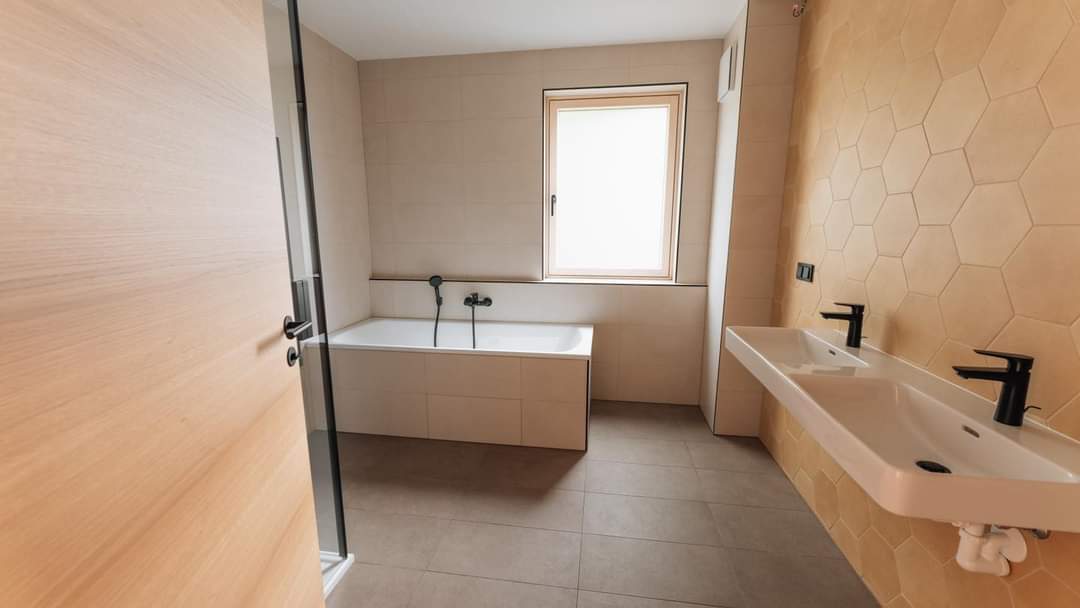 Modernes Badezimmer mit Badewanne, Doppelwaschbecken und hexagonalen Wandfliesen, natürliche Beleuchtung durch Fenster.