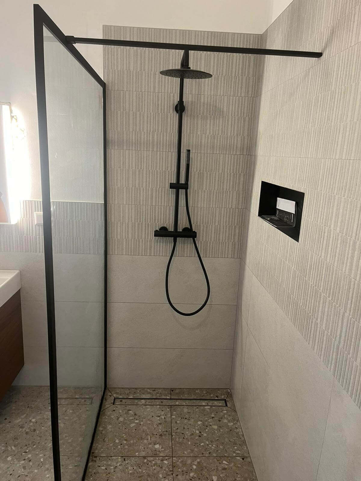 Moderne, elegante Duschkabine mit schwarzer Armatur und Glastrennwand in neutralen Tönen.