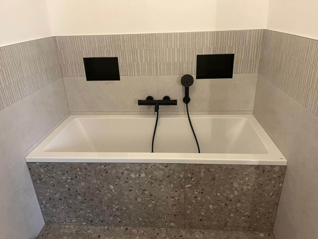 Moderne Badewanne mit stilvoller schwarzer Armatur und eleganten Fliesen in einem minimalistischen Badezimmer.