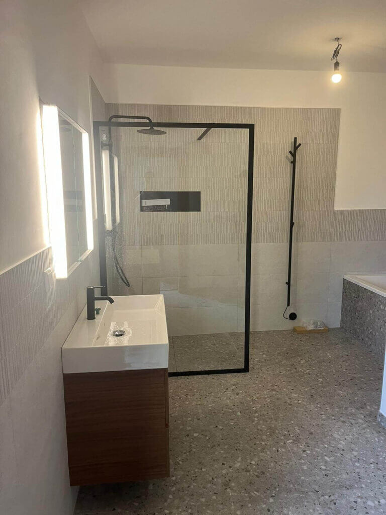Modernes Badezimmer mit begehbarer Dusche, Holzwaschtisch und neutralen Fliesen für minimalistisches Design.