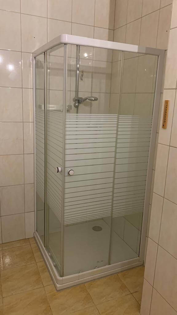 Eckdusche mit Glaswänden und Schiebetür in einem gefliesten Badezimmer, geeignet für moderne Badgestaltung.