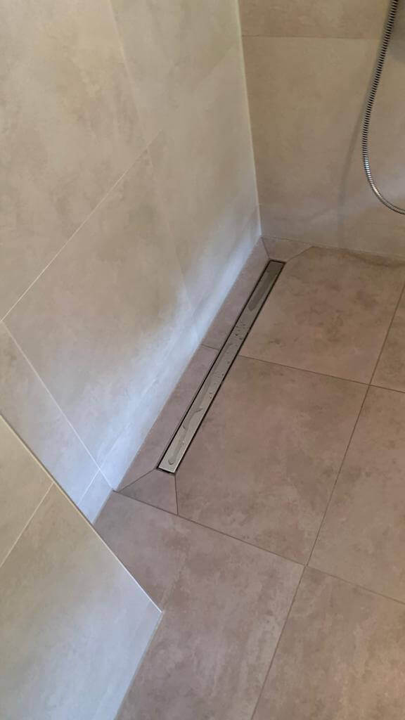 Begehbare Dusche mit neutralen Fliesen und linearer Ablaufrinne für modernes Bad-Design.