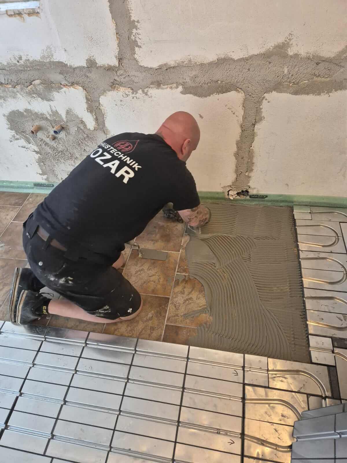 Installateur verlegt Fliesen für Bodenheizung in Badrenovierung, Sanitärdienstleistungen und Reparaturen.